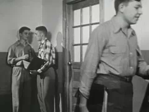Two students standing in hallway talking while others pass by.
