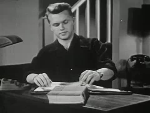Teenage boy sitting at a desk with a large book, stretching in 1950s room.