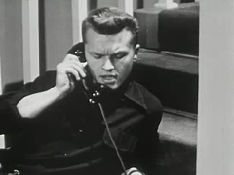 Teenager lying on floor steps, talking angrily on black vintage telephone.