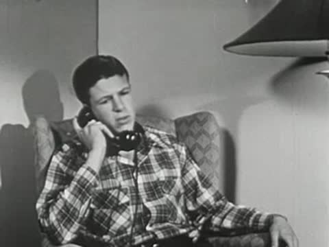 Boy in plaid shirt sitting in armchair while talking on telephone.