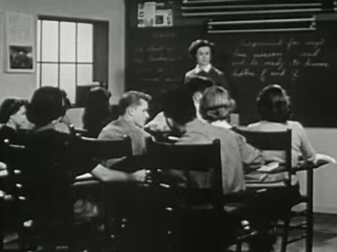 Students sitting at wooden desks in a classroom listening to teacher.