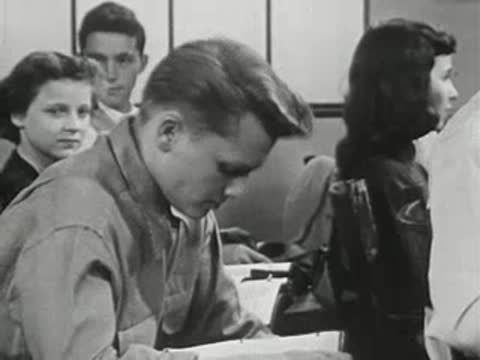Teenage boy sitting at desk in classroom, looking down at his book.
