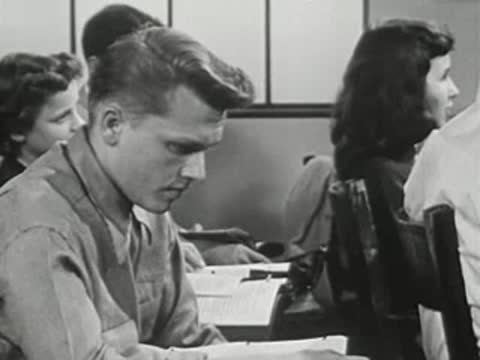 Teen boy studying at desk in classroom, looking down intently.