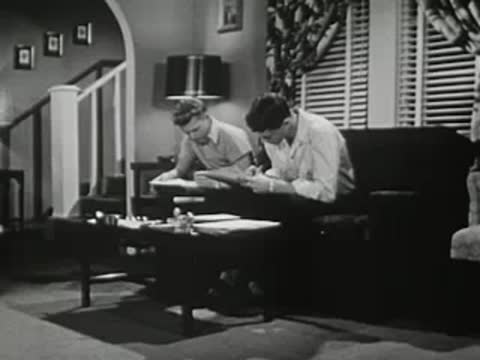 Two teenage boys sitting together at a table studying and writing notes.