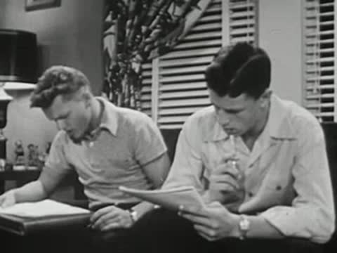 Two young men sitting together at table studying and writing notes.