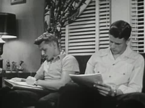 Two young men sitting on couch, reviewing notes and turning pages.