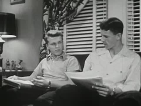 Two young men talking while sitting together on couch with notebooks.