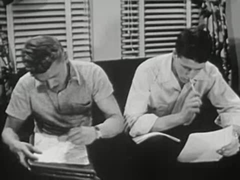 Two young men sitting on couch writing in notebooks together.