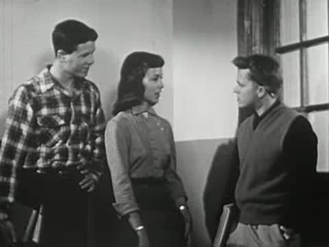 Three teenagers standing together in a hallway talking to each other.