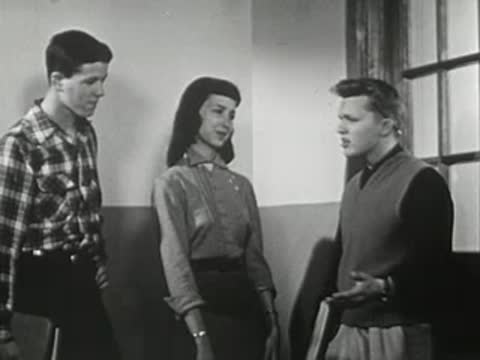 Three teenagers standing together in hallway as another person walks past.
