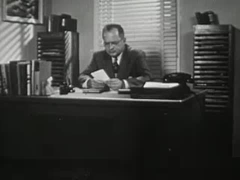 Man in suit sitting at office desk reading papers.