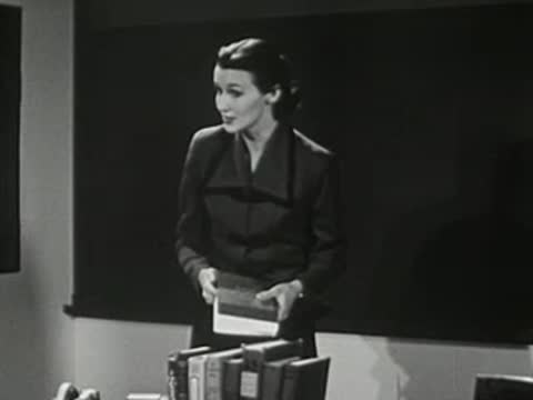 A teacher standing in front of a chalkboard holding books