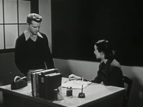 A male student standing next to a female teacher's desk