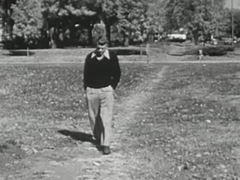 A young man walking on a grassy path through a park