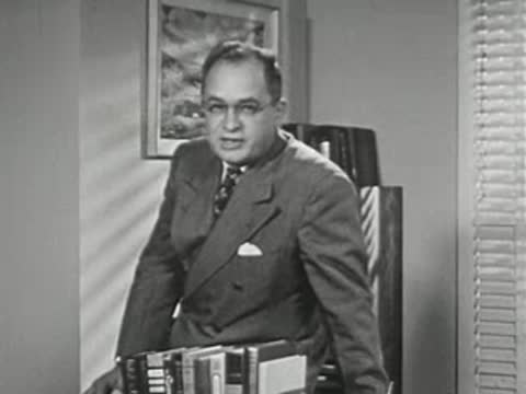 A man in a suit sitting at a desk with books