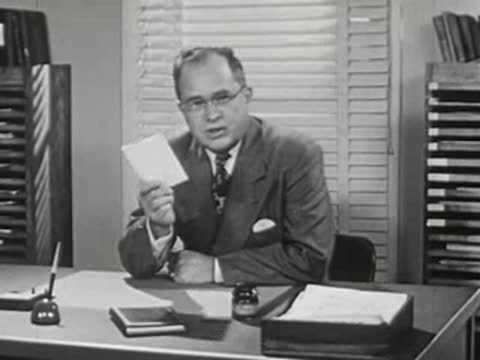 A man in a suit sitting at a desk holding papers