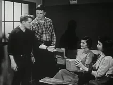 Students gathered around a desk with boxed items in a classroom