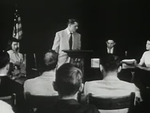 A young man speaking at a podium before a seated audience