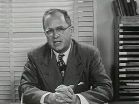 A man in a suit sitting at a desk with folded hands
