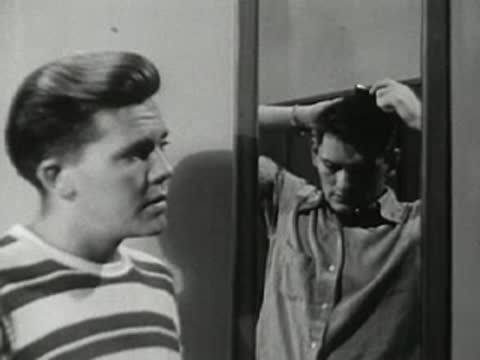 Teen boy looking into mirror and combing his hair in locker room.