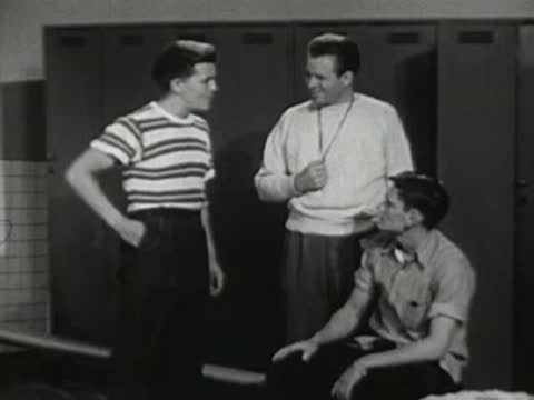 Coach speaking to two boys seated in the locker room.