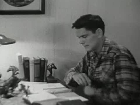 Boy sitting at a desk, writing in a notebook, 1940s classroom.
