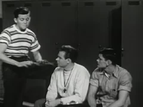 Three young men sitting together indoors, looking and talking.