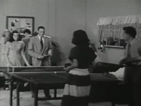 People playing ping pong and socializing in a recreation room.