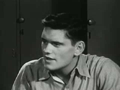 Young man in a shirt sitting and talking, looking sideways.