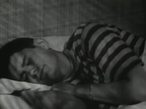 Boy sleeping restlessly in bed under striped covers.