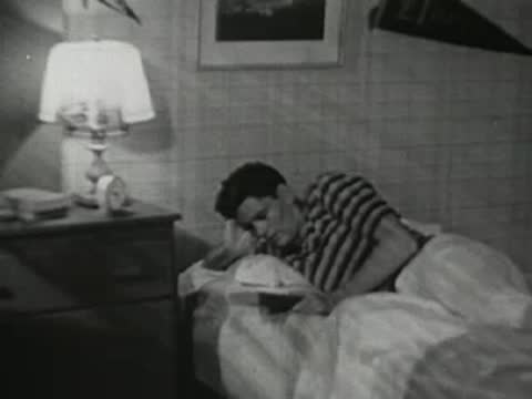 A teenager wakes up in bed, stretches, and reaches to turn off his alarm clock.