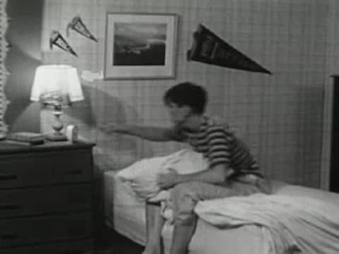 The teenager sits up in bed, stretches, and rubs his face to wake up.