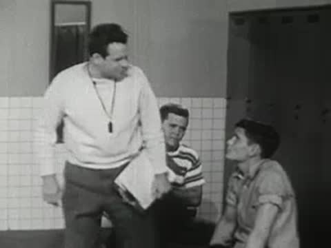 A coach speaks to a couple of athletes in a locker room.