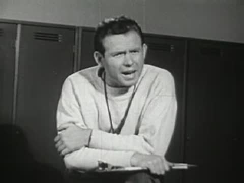 Close-up of the coach speaking seriously with his arms crossed in the locker room.