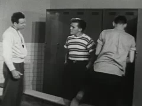 Athletes and coach interacting near lockers in a locker room setting.