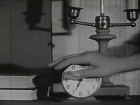 A hand reaches out to turn on an alarm clock on a nightstand.