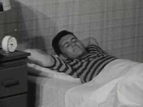 The teenager wakes up in bed, stretching his arms up.