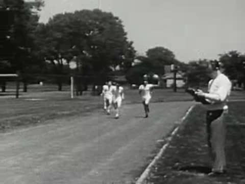 Runners race on a track as a coach times them.