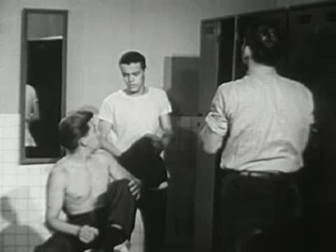 Several teenage boys change clothes inside a school locker room.