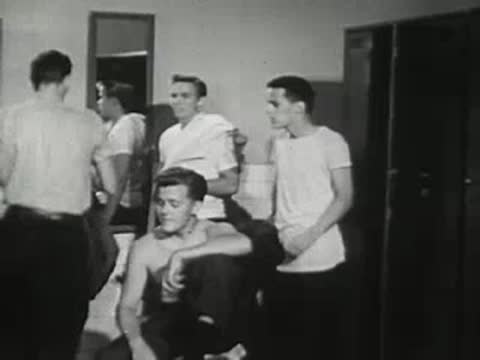 Teenage boys interact while changing clothes in a locker room.