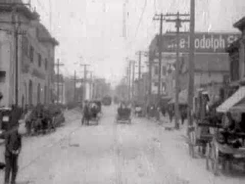 Straight view down a city street with pedestrians and horse-drawn carriages.