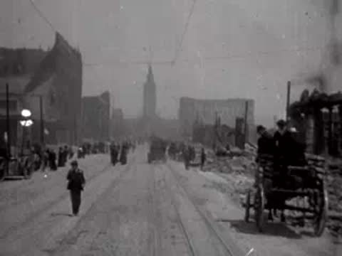 Horse-drawn carriage moving toward the camera on a ruined city street with people.