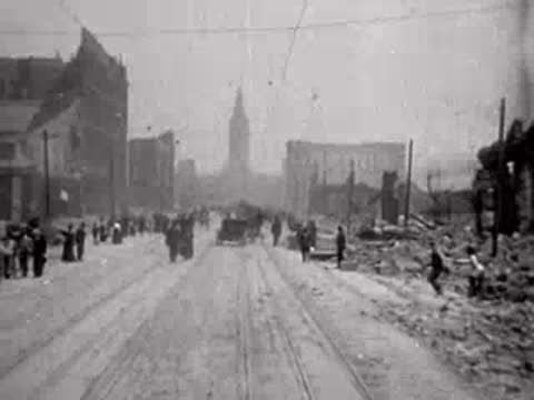 Wide view of a busy ruined street with pedestrians and distant horse-drawn vehicles.