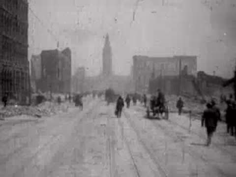 People walking on a ruined city street with debris piles on the sides.
