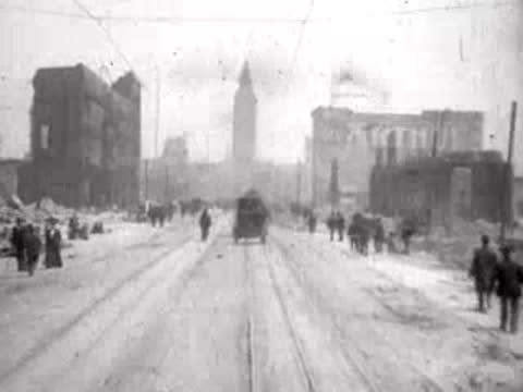 People walking along a wide, debris-strewn avenue in the ruined city.