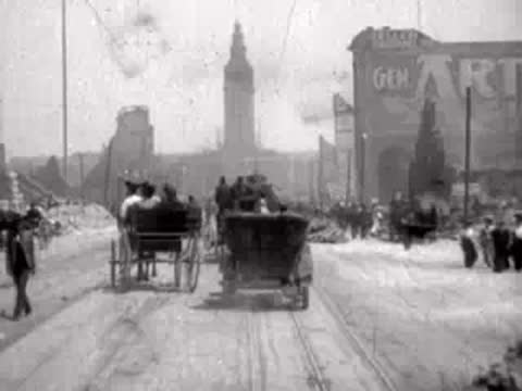 Horse-drawn carriages move down a dusty, rubble-strewn street past ruined buildings.