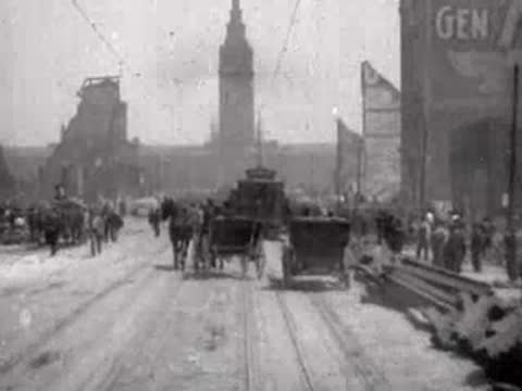 Carriages and crowds of people move through a ruined street in post-earthquake San Francisco.