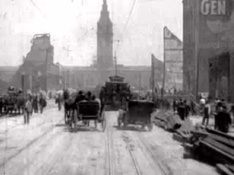 Horse carriages and pedestrians traverse a debris-filled street toward a distant tower.