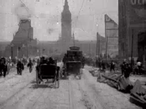 A carriage drives along a rubble-lined street with people walking amidst earthquake ruins.