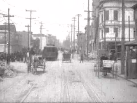 Traffic and pedestrians on a city street flanked by two-story buildings.